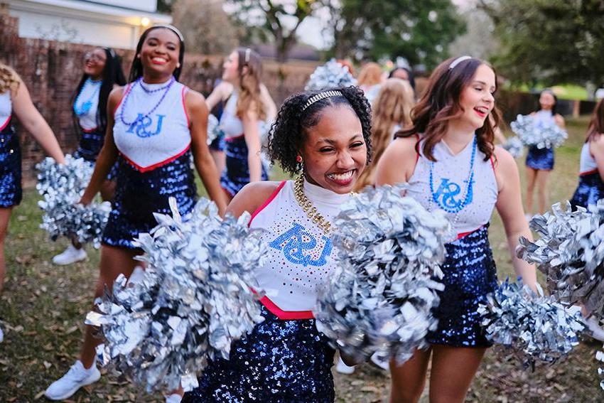 The cheerleader smiling with her pom poms during Mardi Gras Celebration